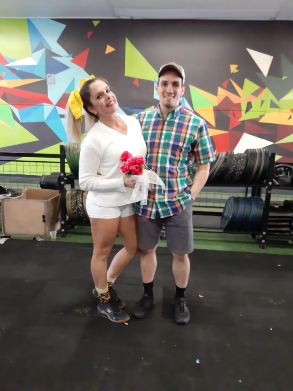 Lyginha vestida de noivinha de Festa Junina, com buquê de rosas, ao lado de André no CrossFit