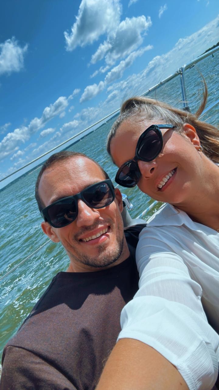 Selfie sorridente de André e Lyginha em um barco, com céu azul ao fundo